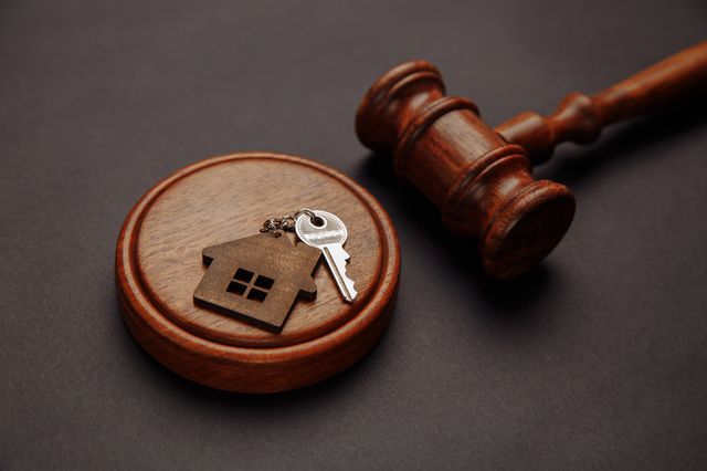 image of a key on a keychain that has a house, sitting atop of a gavel